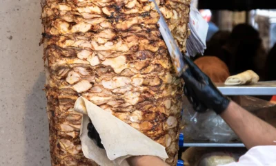 Shawarma chef using a knife to shave chicken shawarma off of a vertical rotating spit